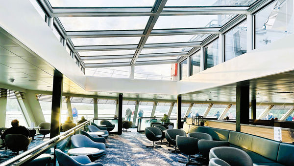 Large windows and a glass ceiling in the lounge of Havila Voyages' Pollux showcase views of the fjords.
